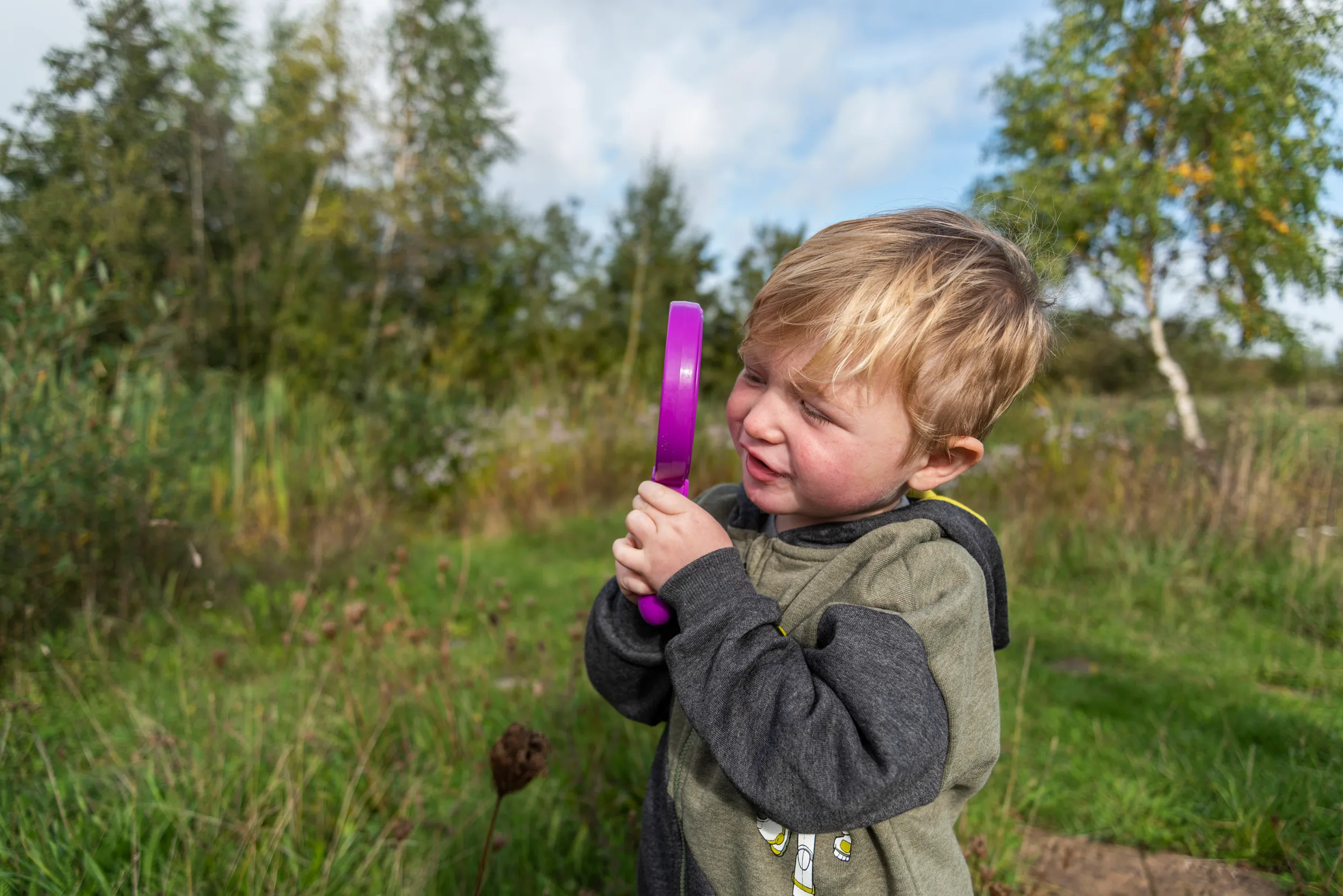 A child stood in woodlands using a purple magnifying glass.